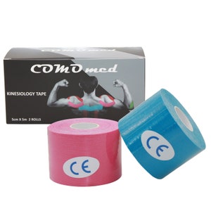 Op de afbeelding: Twee rollen kinesiologietape, een roze en een blauwe, met een CE-markering op elke rol. De tape is 5 cm breed en 5 m lang. De tape is verpakt in een zwarte doos met de merknaam "COMD med" en de woorden "KINESIOLOGY TAPE" en "5cm X 5m 2 ROLLS".