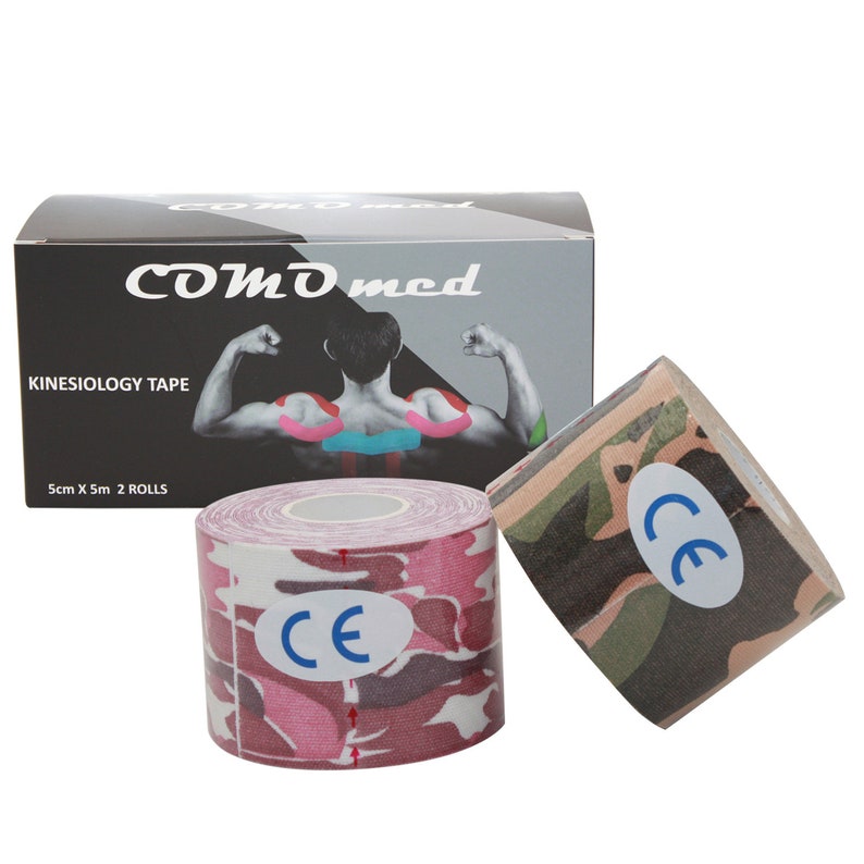 Op de afbeelding: Twee rollen roze en groene camouflage kinesiologie tape. De tape is 5 cm breed en 5 m lang. De doos heeft de tekst "COMD med Kinesiology Tape 5cm X 5m 2 ROLLS" en toont een afbeelding van een persoon met tape op de rug.