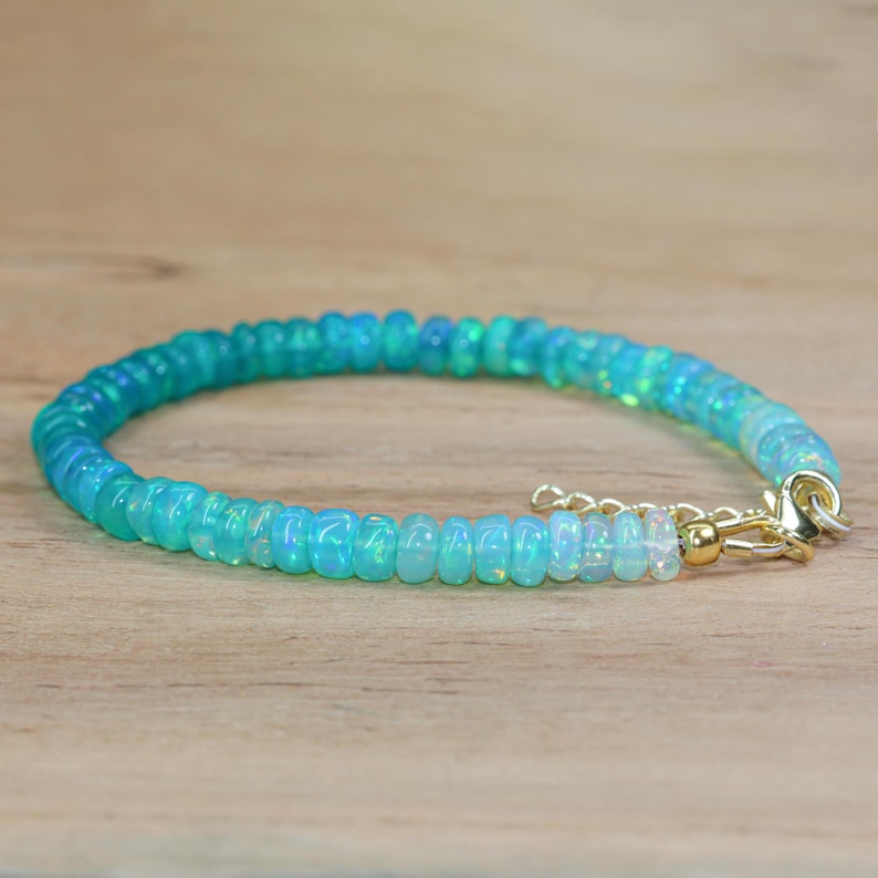 May include: A delicate bracelet made with small, round, light blue and white opal beads. The bracelet has a gold clasp.