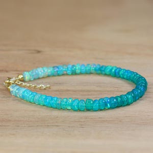 May include: A delicate opal beaded bracelet with a gradient of light blue to dark blue beads. The bracelet is made with gold-toned metal clasps.