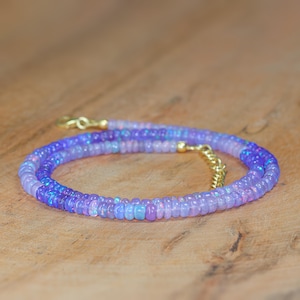 May include: A delicate necklace made of small, iridescent purple opal beads. The necklace is layered and features a gold clasp.