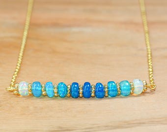 May include: A gold chain necklace with a graduated row of blue and white opal beads. The beads are arranged in a gradient from white to blue.