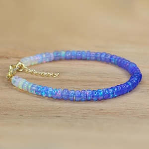 May include: A delicate bracelet made with small, iridescent opal beads. The beads are graduated in color, starting with white and transitioning to a light blue.