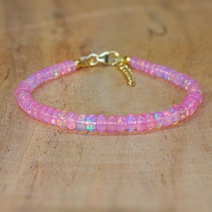 Könnte beinhalten: Ein zartes Armband aus rosa Opal mit einem goldenen Verschluss. Das Armband besteht aus kleinen, runden Perlen, die zu einem einfachen und eleganten Design zusammengefügt sind.