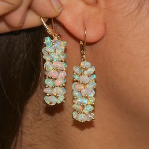 May include: A pair of gold dangle earrings with a cluster of iridescent white opal beads. The earrings are long and delicate, with a simple hook closure.