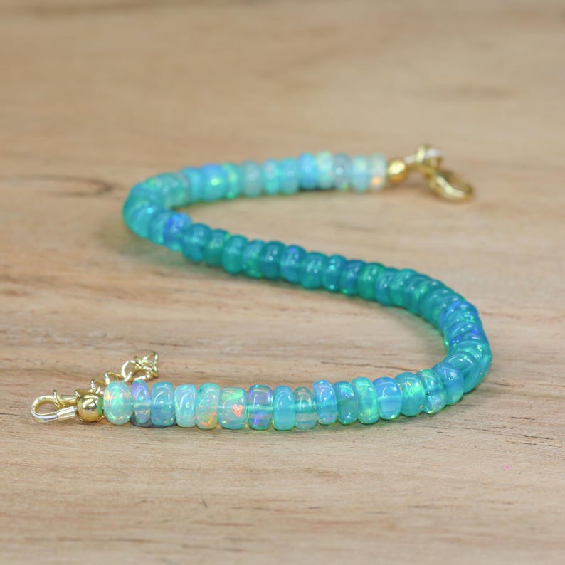 May include: A delicate bracelet made with graduated opal beads in shades of light blue and white. The bracelet features a gold clasp and extender chain.