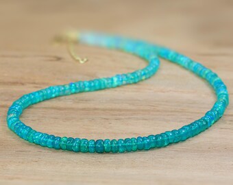 May include: A turquoise opal beaded necklace with a gold clasp. The necklace is on a wooden surface.