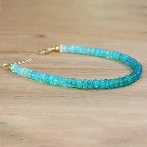 May include: A delicate necklace made of light blue and white opal beads. The necklace has a gold clasp and is perfect for adding a touch of elegance to any outfit.