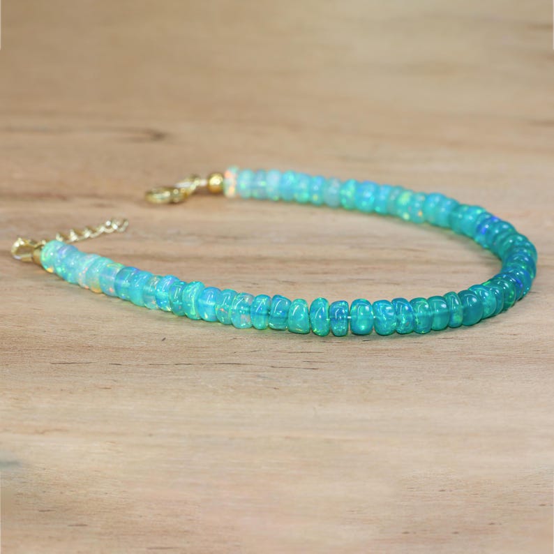 May include: A delicate necklace made of light blue and white opal beads. The necklace has a gold clasp and is perfect for adding a touch of elegance to any outfit.