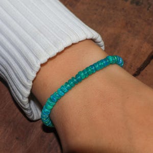 May include: A turquoise blue opal beaded bracelet on a person's wrist.