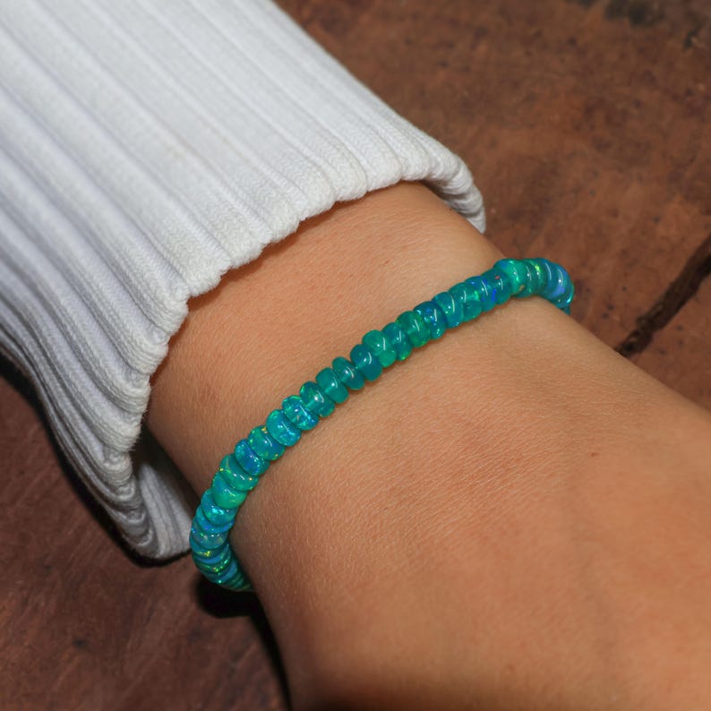 May include: A turquoise blue opal beaded bracelet on a person's wrist.