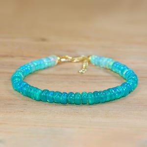 May include: A delicate bracelet made with light blue and white opal beads. The bracelet has a gold clasp.