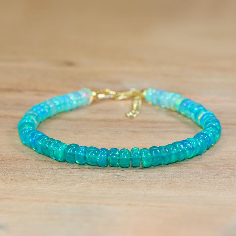 May include: A delicate bracelet made with light blue and white opal beads. The bracelet has a gold clasp.