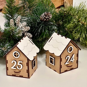 May include: Two wooden Christmas countdown houses with white roofs. The house on the left has the number 25 on the front and the house on the right has the number 24 on the front.