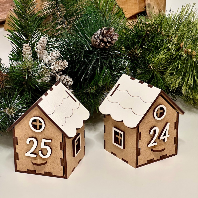 May include: Two wooden Christmas countdown houses with white roofs. The house on the left has the number 25 on the front and the house on the right has the number 24 on the front.