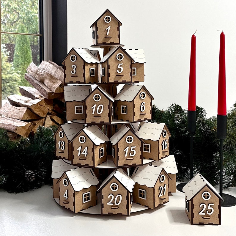 May include: A wooden Christmas advent calendar shaped like a Christmas tree with 25 numbered doors. Each door is a small house with a white roof. The calendar is on a white surface.