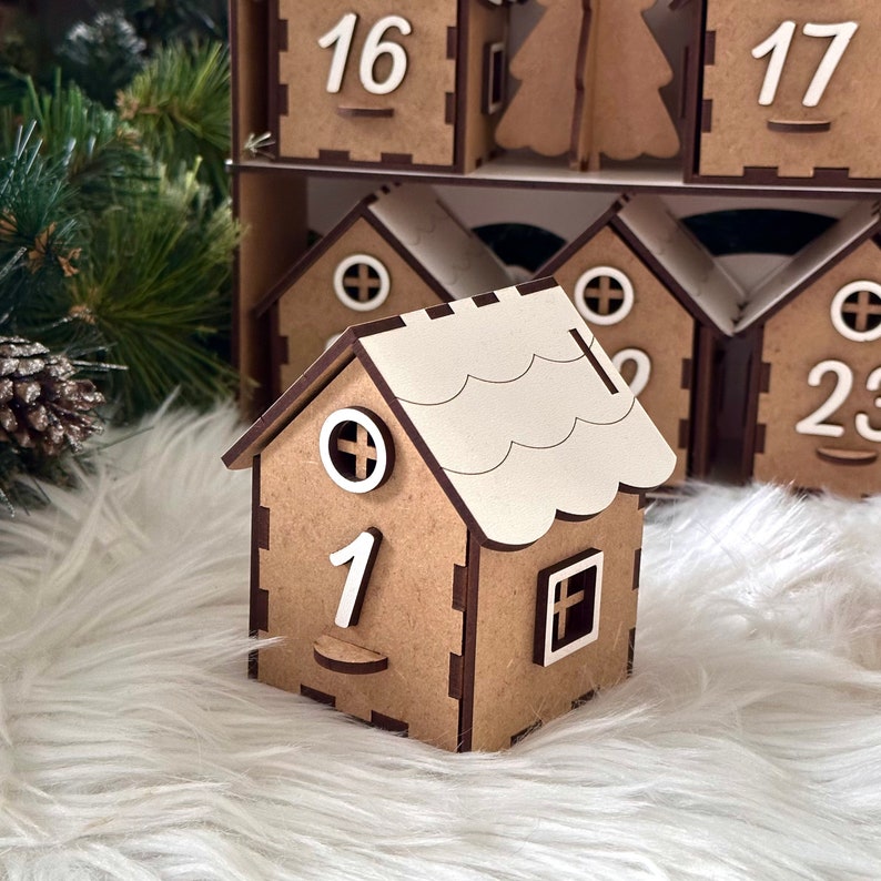 May include: A wooden advent calendar shaped like a house with a white roof. The house has a small window and the number "1" on the front. The calendar is made of brown wood and has a rustic look.