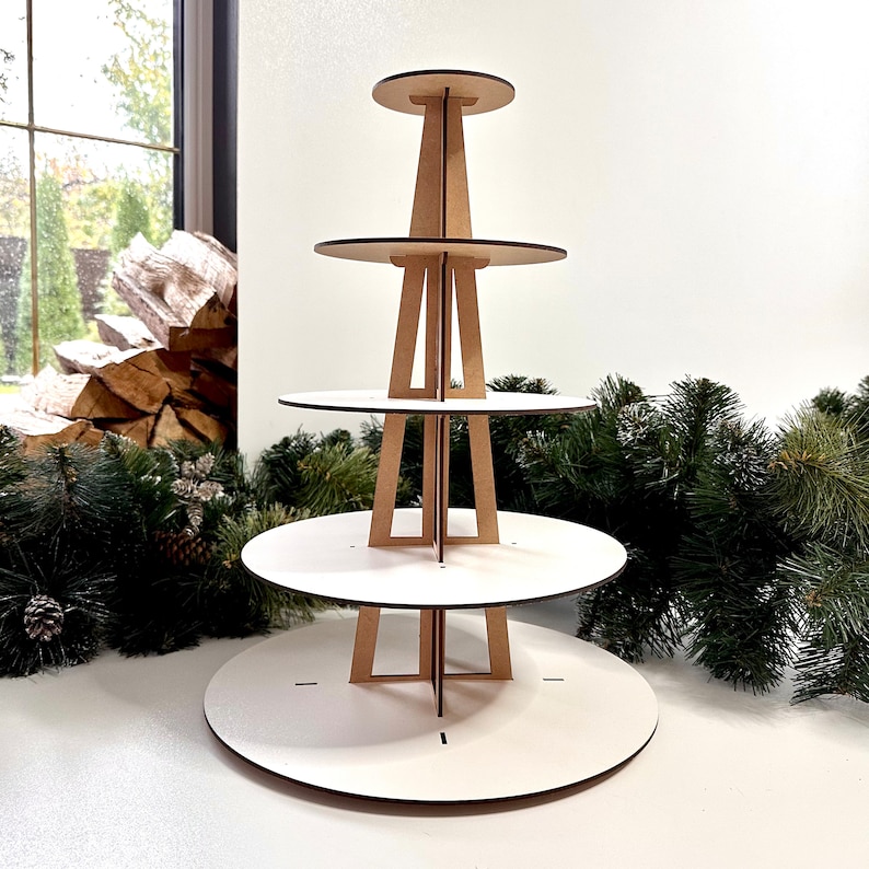 May include: A white four-tiered cupcake stand made of wood. The stand is designed to hold cupcakes or other small desserts. It is a great way to display your baked goods at a party or event.