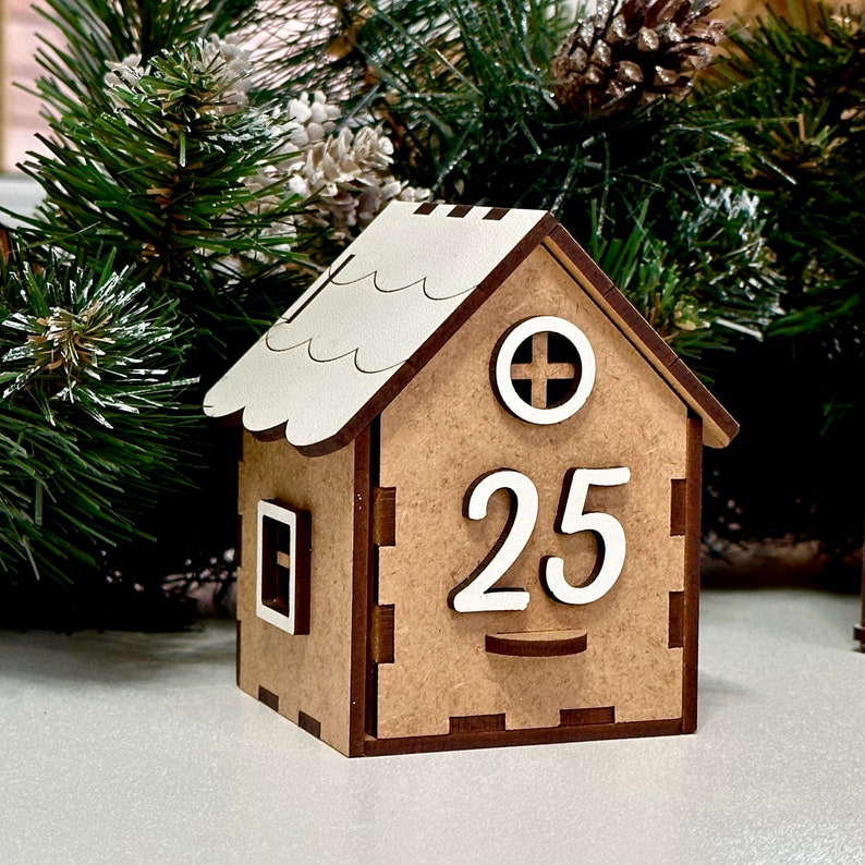 May include: A wooden house-shaped advent calendar with a white roof and a number 25 on the front. The house is brown with a white window and a white circle with a plus sign.