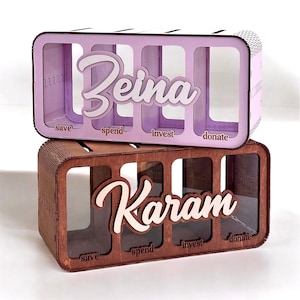 Puede incluir: Dos cajas de dinero de madera con ranuras etiquetadas como "save", "spend", "invest" y "donate". La caja superior es de color morado claro con el nombre "Beina" escrito en blanco. La caja inferior es de color marrón con el nombre "Karam" escrito en blanco.