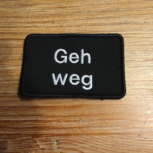 Könnte beinhalten: Schwarzer Stoff-Patch mit weiß gesticktem Text "Geh weg".