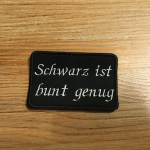 Könnte beinhalten: Schwarzer gestickter Aufnäher mit weißem Text, der "Schwarz ist bunt genug" lautet.