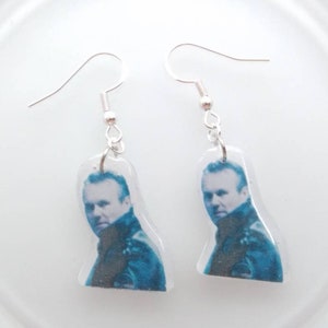 May include: A pair of silver dangle earrings with a clear resin charm featuring a black and white photo of a man.