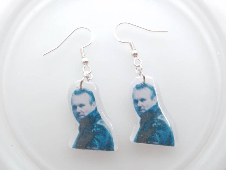 May include: A pair of silver dangle earrings with a clear resin charm featuring a black and white photo of a man.