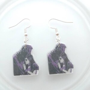 May include: A pair of silver dangle earrings with a purple and black image of a couple embracing. The image is printed on a clear plastic charm.