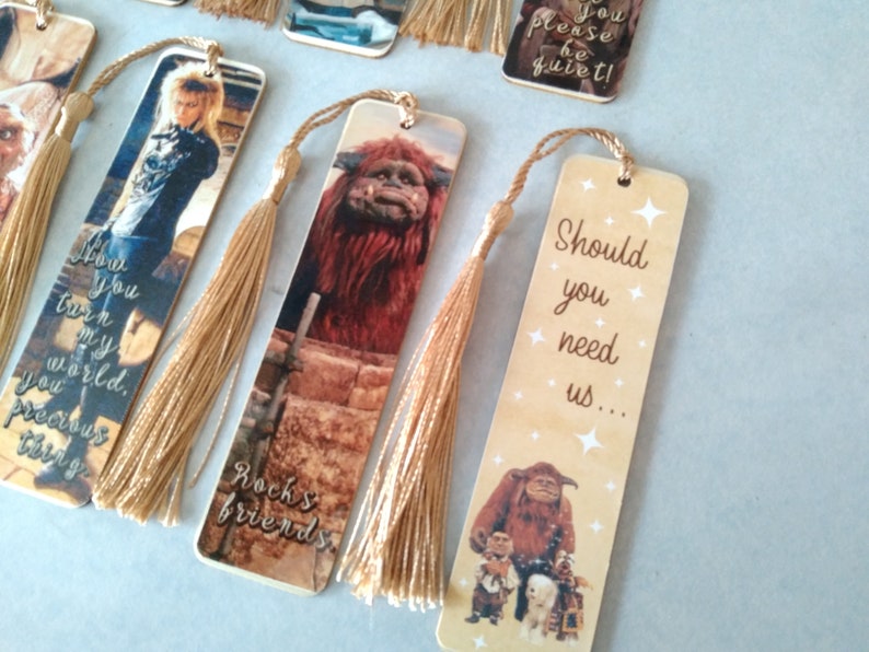 K&ouml;nnte beinhalten: Satz von sechs Holz-Lesezeichen mit Bildern und Zitaten aus dem Film Labyrinth. Die Lesezeichen haben goldene Quasten. Die Zitate lauten: "You turn my world, you precious thing", "Rock's friends", "You please be quiet!" und "Should you need us..."