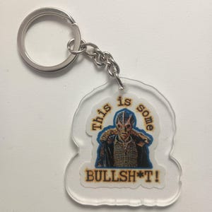 May include: A clear acrylic keychain with a printed image of a man in a blue jacket and the text "This is some BULLSH*T!"