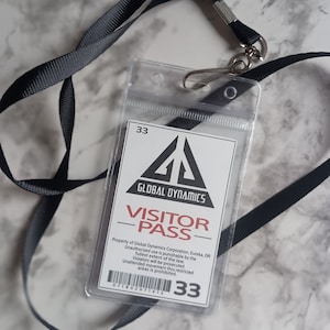 May include: A white visitor pass with a black triangle logo that says "Global Dynamics". The pass has the text "Visitor Pass" in red and black. The pass also has the text "Property of Global Dynamics Corporation, Eureka, OR" and "Unauthorized use is punishable by the fullest extent of the law. Violators will be prosecuted. Unattended movement thru restricted areas is prohibited." The pass has a barcode and the number "33" printed on it.