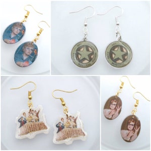 May include: A collection of novelty earrings featuring various designs. The earrings include images of a woman, a star emblem, and a group of people. The earrings have gold or silver-colored hooks.