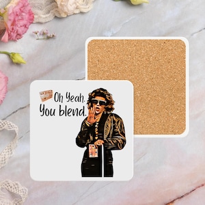 Puede incluir: Posavasos de cerámica blanca con respaldo de corcho. El posavasos presenta una imagen de dibujos animados de una mujer con gafas de sol y una chaqueta de cuero negra. El texto "Oh Yeah. You blend." está impreso en el posavasos.