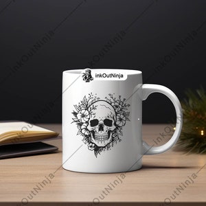 May include: White ceramic mug with a black and white illustration of a skull surrounded by flowers. The mug has a black handle and the text "inkOutNinja" is printed on the side.