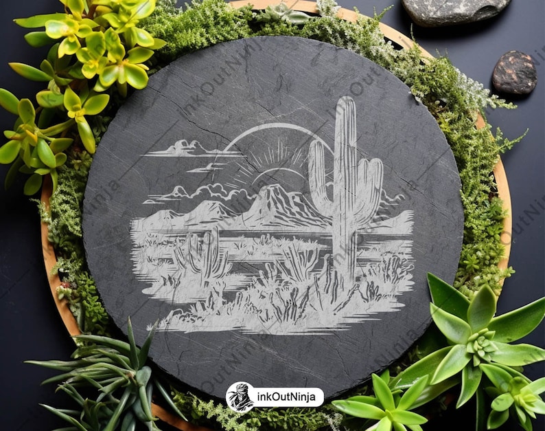 May include: A black slate coaster with a white etched design of a desert landscape with a large cactus and a rising sun. The coaster is surrounded by green plants.