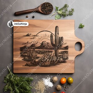 May include: A wooden cutting board with a laser-engraved design of a desert landscape with a cactus and a rising sun. The board has a handle on the side.
