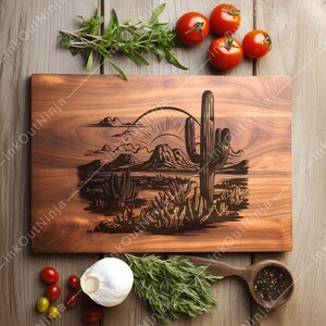 May include: A wooden cutting board with a laser-engraved design of a desert landscape with a cactus and a mountain range. The sun is setting behind the mountains.