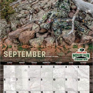 May include: A 2026 Mossy Oak Mountain Country calendar featuring a camouflage-clad person with a bow and arrow in a rocky, wooded setting. The September calendar page is visible, with a wooden textured border.