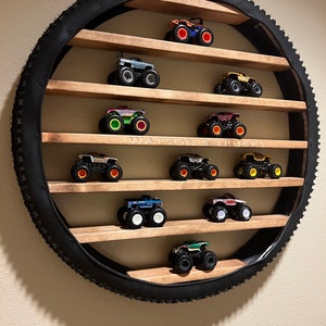 May include: A circular shelf made from a tire with wooden shelves. The shelves are filled with toy monster trucks in various colors. The text "WATSON'S TRUCKS" is printed on the shelf.