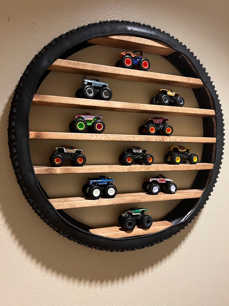 May include: A circular shelf made from a tire with wooden shelves. The shelves are filled with toy monster trucks in various colors. The text "WATSON'S TRUCKS" is printed on the shelf.