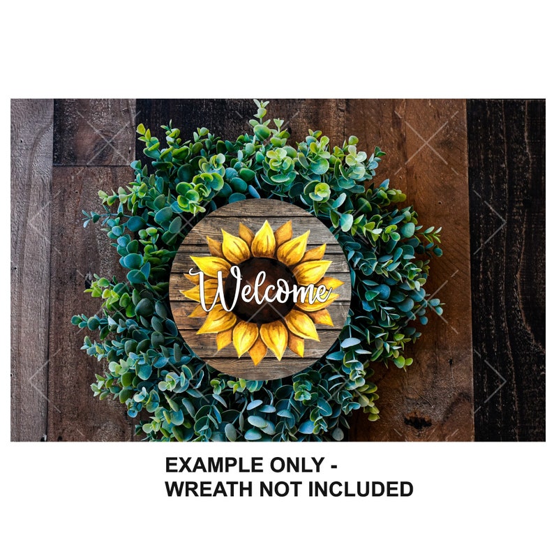 K&ouml;nnte beinhalten: Ein rundes Holzschild mit einer gemalten Sonnenblume und dem Wort "Willkommen" in wei&szlig;en Buchstaben. Das Schild ist auf einem gr&uuml;nen Kranz angebracht.
