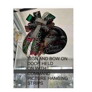 a sign and bow hanging on a door, with the sign displaying a Santa Claus image and the bow featuring a Christmas-themed design.
