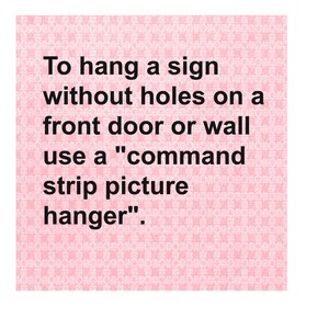 May include: A pink background with the text: "To hang a sign without holes on a front door or wall use a 'command strip picture hanger'." The text is in black.