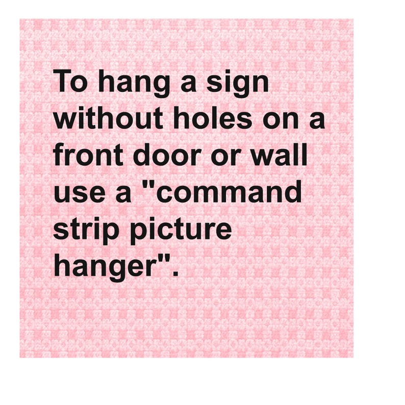 May include: A pink background with the text: "To hang a sign without holes on a front door or wall use a 'command strip picture hanger'." The text is in black.