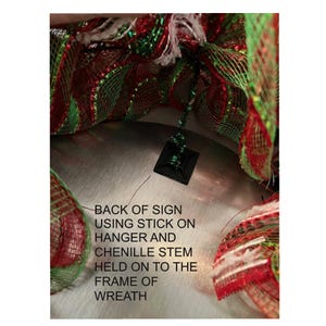 a close-up view of a Christmas wreath made of colorful mesh material, with a black sign attached to it.