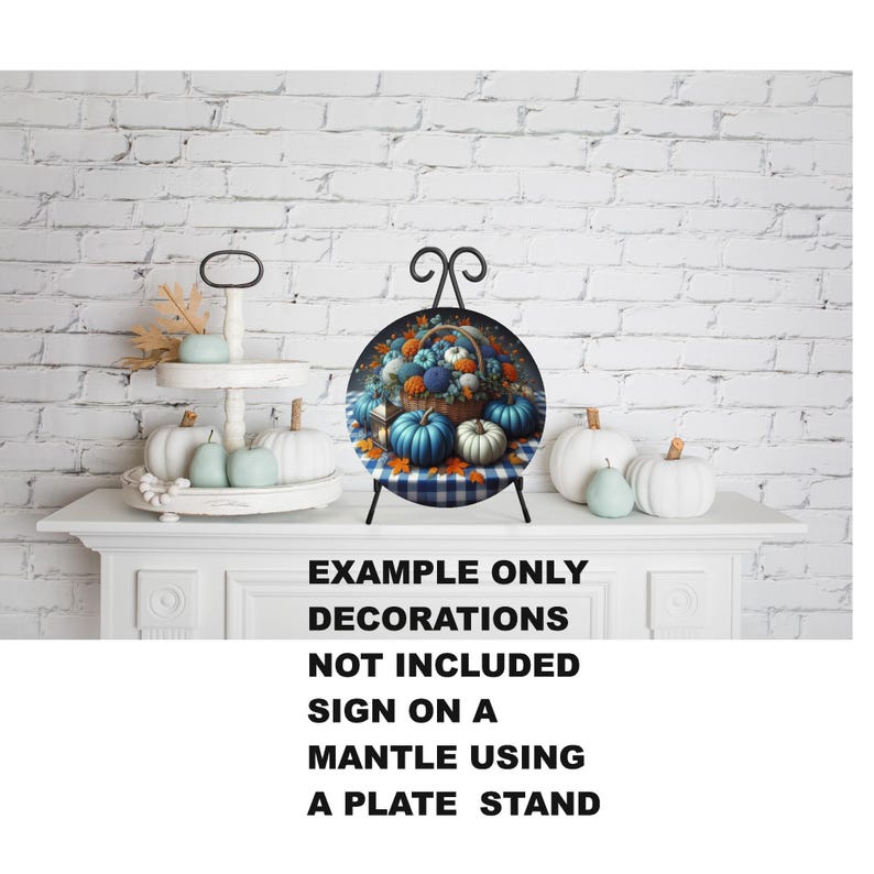 May include: A decorative plate featuring a basket of pumpkins and flowers, displayed on a black plate stand. The plate is set against a white brick wall, with additional pumpkins and a tiered tray with pumpkins. The text on the image reads: EXAMPLE ONLY, DECORATIONS NOT INCLUDED, SIGN ON A MANTLE USING A PLATE STAND.
