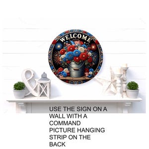a decorative sign with a patriotic design, including a bucket filled with flowers and fireworks, mounted on a wall above a white shelf.