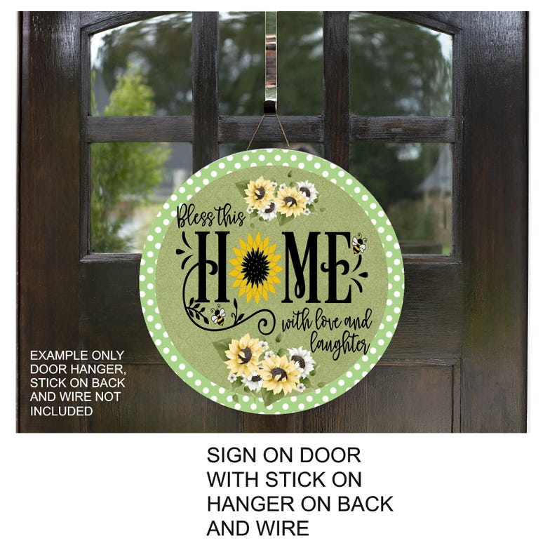 May include: Round wooden sign with a green background and white polka dots. The sign features a sunflower, the word "HOME", and the phrase "Bless this Home with love and laughter". Includes a wire hanger.