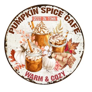 K&ouml;nnte beinhalten: Ein rundes Metallschild mit wei&szlig;em Hintergrund und braunen, abgenutzten R&auml;ndern. Das Schild zeigt ein rustikales Design mit dem Text "Pumpkin Spice Cafe" in braunen Buchstaben. Der Text "Best in Town" ist in Pink auf einem wei&szlig;en Banner geschrieben. Das Schild zeigt auch eine Aquarell-Illustration von drei Pumpkin Spice Lattes mit Schlagsahne und Zimt sowie K&uuml;rbissen, Herbstbl&auml;ttern und Blumen. Der Text "Warm & Cozy" ist in braunen Buchstaben am unteren Rand des Schildes geschrieben.